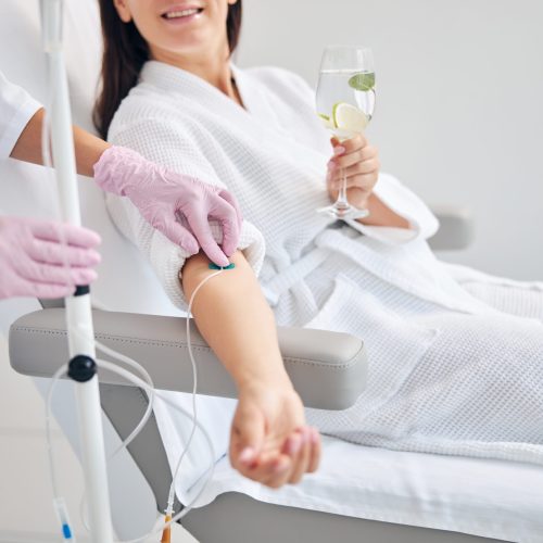 Cropped photo of a woman with a glass of drink sitting in a cosmetic chair